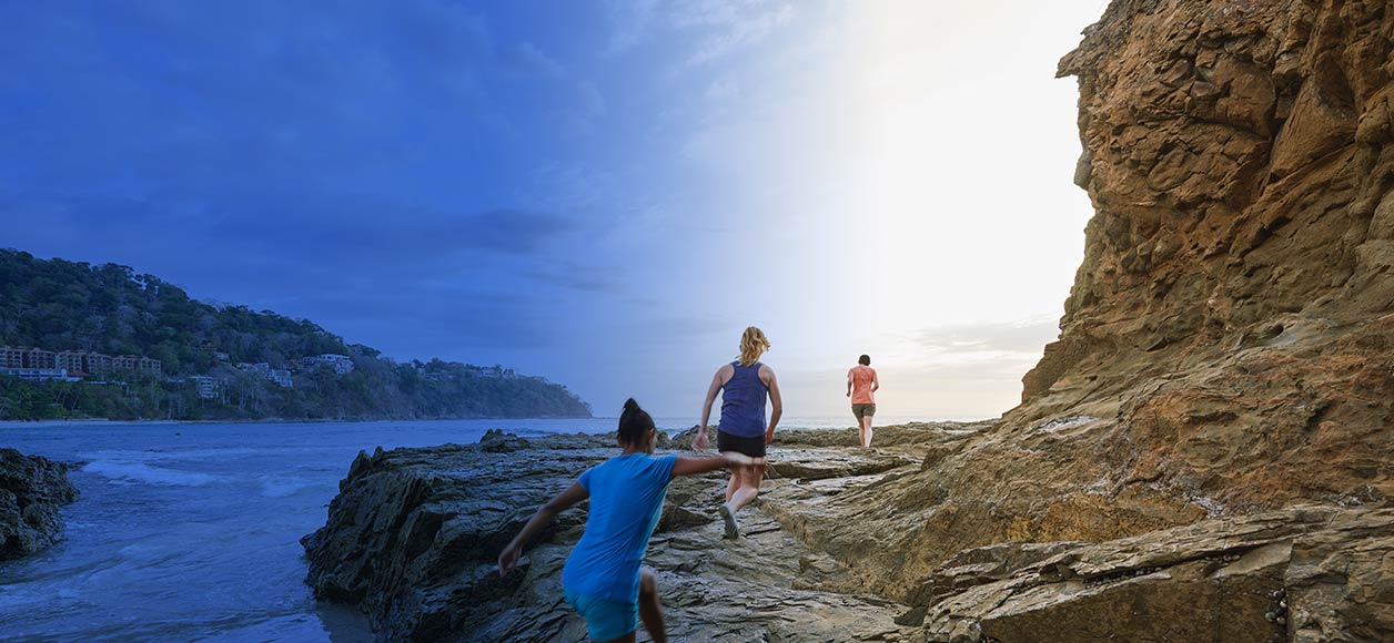 Three people running away over rocks by the ocean.